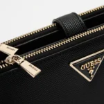 Close-up of a black Guess handbag with gold zippers and textured surface.