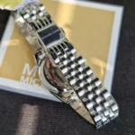 Close-up of a silver Michael Kors wristwatch with a linked metal bracelet, resting on a Michael Kors box.