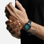 omega-seamaster-aqua-terra-150m-co-axial-master-chronometer-41mm-automatic-men_4 Teal dial wristwatch on a man's left wrist with a black strap and silver case, close-up view.