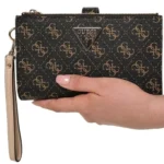 Black Guess clutch wallet with a tan monogram pattern held in a hand, beige wrist strap attached on the left.