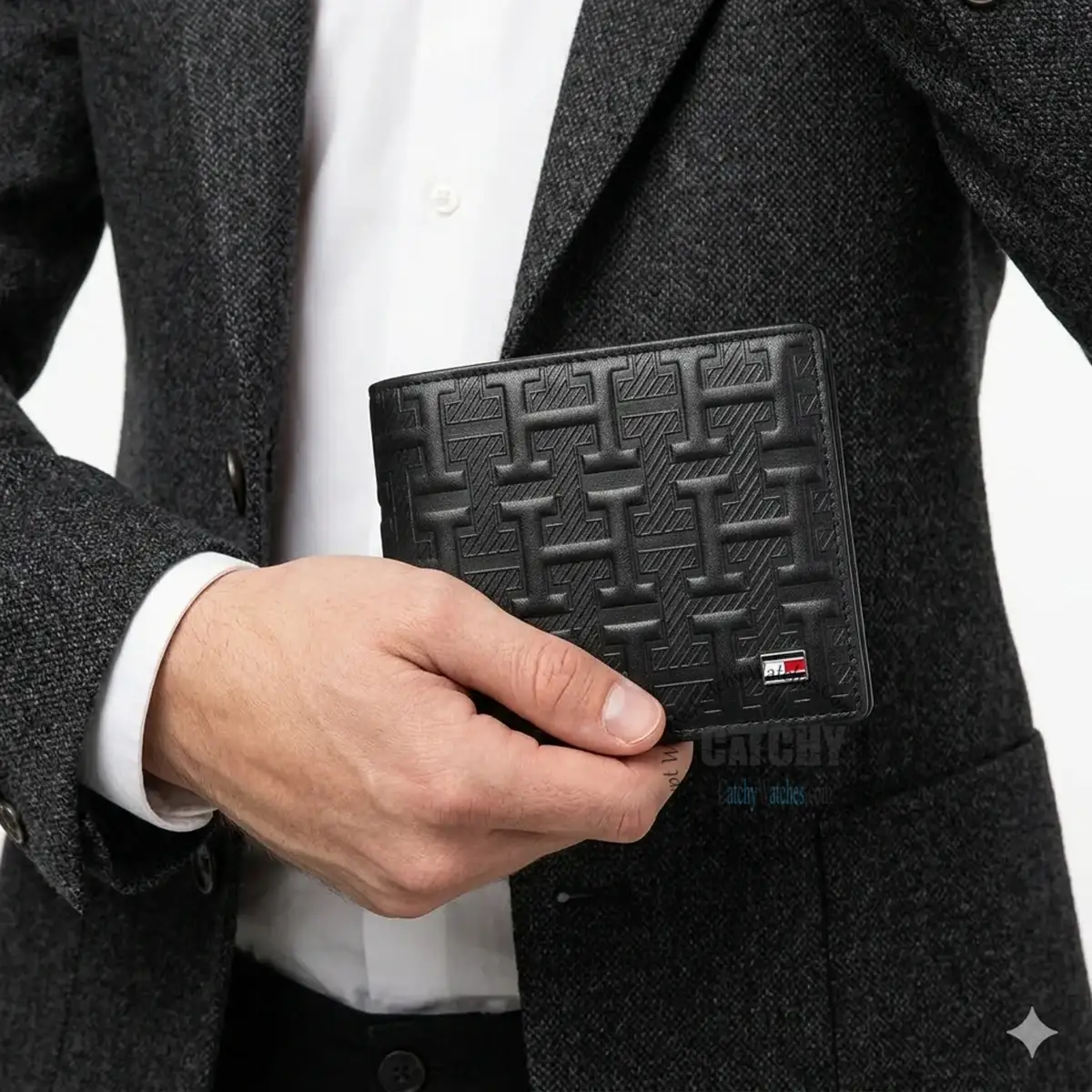 Man in a dark blazer holding a black embossed wallet with a small logo on the corner side.