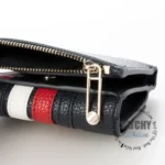 original-tommy-hilfiger-wallet-women-navy-blue-genuine-leather_7 Close-up of a black leather bag showing a gold zipper and red, white, and black stitched strap detail.