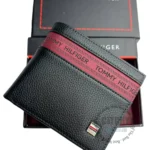 original-wallets-gifts-box-black-logoth-genuine-leather_2 Black pebbled leather wallet with a red Tommy Hilfiger stripe across the front, resting on a branded box.