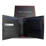 original-wallets-gifts-box-black-logoth-genuine-leather_3 Black pebbled leather wallet opened to show card slots, with a Tommy Hilfiger box in the background.