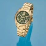 Gold-tone Michael Kors chronograph wristwatch with a green dial and multiple subdials on a blue background.