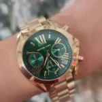 Gold Michael Kors wristwatch with a green dial and multiple subdials, worn on the wrist.