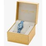 Blue Michael Kors watch with metal bracelet nestled in a gold textured gift box with a pale interior cushion.