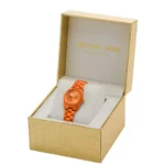 Orange Michael Kors wristwatch in gold textured box on white cushion, showing a stylish display.