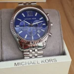 mk8280-michael-kors-watch-men-blue-dial-metal-stainless-steel-silver-strap-quartz-battery-analog-chronograph-lexington_105 Michael Kors wristwatch with blue dial and silver band, displayed on a cushioned stand in a box labeled MICHAEL KORS.