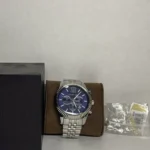 mk8280-michael-kors-watch-men-blue-dial-metal-stainless-steel-silver-strap-quartz-battery-analog-chronograph-lexington_109 Michael Kors stainless steel chronograph watch with blue dial on a brown display cushion beside a black box.