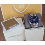 mk8280-michael-kors-watch-men-blue-dial-metal-stainless-steel-silver-strap-quartz-battery-analog-chronograph-lexington_110 Michael Kors watch with blue dial displayed on a gray cushion, surrounded by brand boxes and a yellow Michael Kors bag in the background