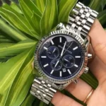 mk8280-michael-kors-watch-men-blue-dial-metal-stainless-steel-silver-strap-quartz-battery-analog-chronograph-lexington_9 Stainless steel chronograph watch with a blue dial held against green plant leaves.