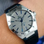 Omega Constellation wristwatch on a blue strap with a brushed silver dial, blue hour markers, and a date window at 3 o'clock.