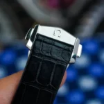 Close-up of a silver watch clasp with an Omega logo on a black alligator-embossed leather strap.