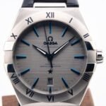 Close-up of a stainless steel Omega Constellation watch face with blue baton markers and a date window at 6 o'clock.