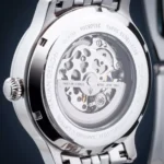 Close-up of a polished stainless steel watch case back revealing the intricate mechanical movement and gears inside.