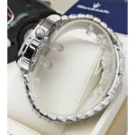 Close-up of a silver stainless steel wristwatch on a display cushion, showing the crown with a logo and polished links in the bracelet.