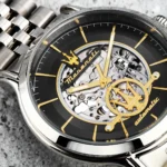 Close-up of a skeleton wristwatch with gold hands and a visible mechanical movement, black dial with gold markers and a Maserati trident emblem.