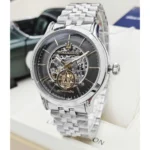 Silver skeleton automatic wristwatch with exposed gears, black dial, and gold hour markers, featuring a Maserati emblem at the center and a metal bracelet.