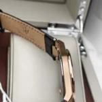 r8851153001-original-maserati-watch-men-black-dial-leather-strap_16 Close-up of a rose-gold wristwatch with a tan leather strap in a display case.