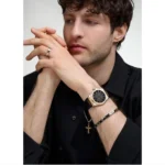 r8851153001-original-maserati-watch-men-black-dial-leather-strap_8 Man in a black shirt with hands clasped, wearing a rose-gold wristwatch, ring and bracelet, plus a cross necklace.