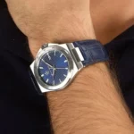 Wristwatch with a blue textured dial, silver case, and blue leather strap on a man’s wrist.