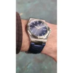 Wrist wearing a stainless steel wristwatch with a blue textured dial and blue leather strap.
