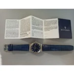 Blue leather‑strap Maserati wristwatch with silver case, placed under an open warranty/information booklet on a gray surface, brand visible.