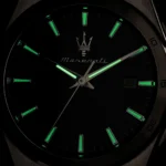 Close-up of a black Maserati wristwatch dial with green luminous hour markers and hands, plus the Maserati trident logo at center.