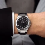 Stainless steel wristwatch with a black textured dial and date window worn on a suited wrist.