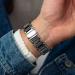 Close-up of a wrist wearing a silver metal watch bracelet over a white knit cuff and denim jacket sleeve.