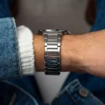 Close-up of a wrist wearing a silver stainless steel watch with a denim sleeve nearby.