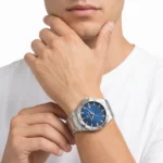 Close-up of a man wearing a silver stainless steel watch with a blue dial on his left wrist, hands near his chin.