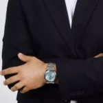 Man in a black blazer crosses his arms, wearing a silver metal wristwatch on his left wrist.