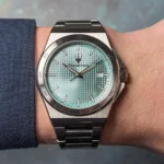 Stainless steel wristwatch with a teal textured dial and date window showing 23, worn on a metal bracelet.