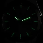 Wristwatch face in darkness with glowing green hour and minute hands and green hour markers. The bezel numbers are faintly visible.