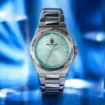 Stainless steel wristwatch with a turquoise grid-pattern dial, date window at 3 o'clock, and a metal link band against a blue background.