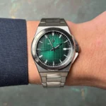 Stainless steel wristwatch with a green textured dial showing time and a date window on a wrist.
