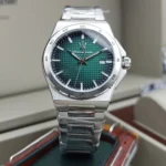 Stainless steel wristwatch with a green textured dial, date window at 3 o'clock, on a display box.