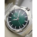 Close-up of a stainless steel wristwatch with a green textured dial, silver markers, and a date window at 3 o'clock.