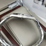 Side view of a silver stainless steel wristwatch with a brushed case and linked bracelet, resting on a padded display in a box.