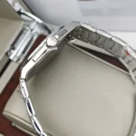 Close-up of a silver stainless steel wristwatch with a crown, resting on a padded display surface in a box.