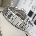 Close-up of a silver stainless steel watch bracelet with a deployment clasp, resting on a light surface with the watch case partly visible in the background.