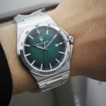 Stainless steel wristwatch with a green textured dial, silver indices, and a date window at 3 o'clock on a metal bracelet.