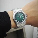 Silver stainless steel wristwatch with a green textured dial and date display on the 3 o'clock position, worn on the wrist.