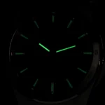 Wristwatch face in darkness with glowing green lume on hour markers and hands.