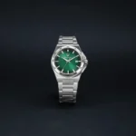 Silver metal wristwatch with a green textured dial and date window against a dark background."