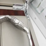 Close-up side view of a silver stainless steel watch with a crown featuring a logo, showing polished links and a curved case edge.