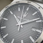 Close-up of a Maserati wristwatch face with a gray grid-pattern dial, white hands, and a date window at 3 o'clock.