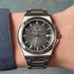 Stainless steel wristwatch on a wrist, black textured dial, date display at 3 o'clock, and metal link bracelet.